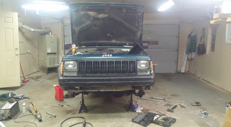 The XJ sits in a garage as its suspension parts are removed.